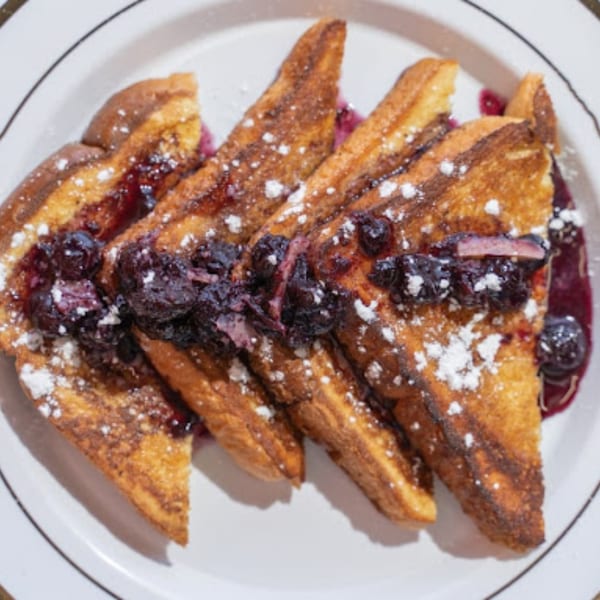 Four slices of golden French toast topped with blueberry compote and powdered sugar on a white plate.