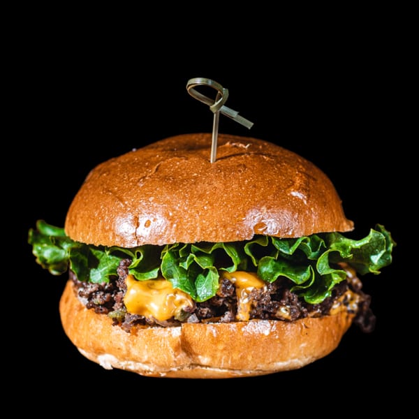 BB's Burger Factory's burger with melted cheese, lettuce, and a skewer on a black background.