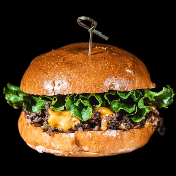 BB's Burger Factory's burger with melted cheese, lettuce, and a skewer, against a black background.