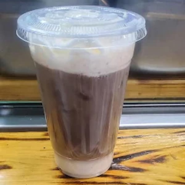 A clear plastic cup filled with a dark brown drink, topped with light foam and a lid.