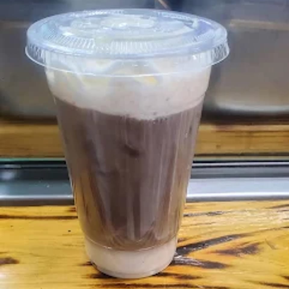 A clear plastic cup filled with a dark brown drink, topped with light foam and a lid.
