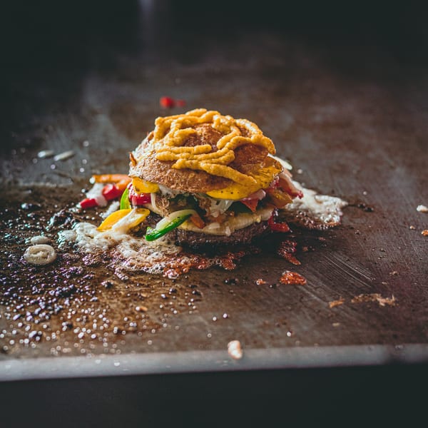 BB's Burger Factory's burger with cheese, peppers, and onions cooking on a sizzling griddle.